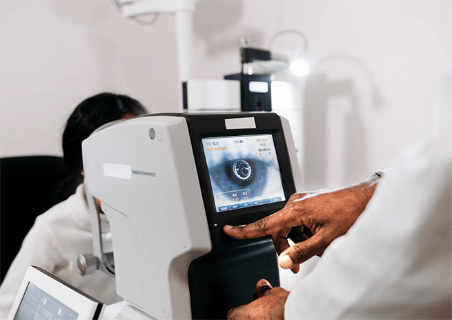 A clinician operating an autorefractor, the patient's eye shown on the screen