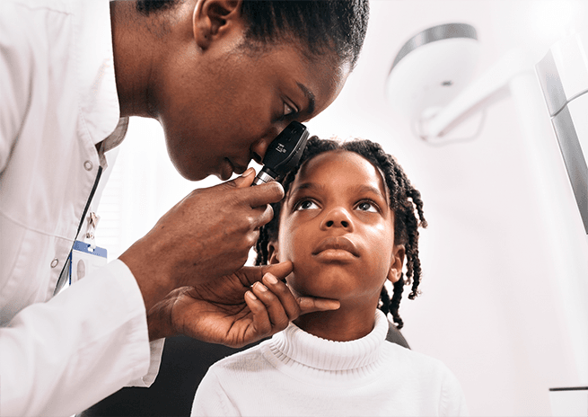 An ophthalmologist examining a young girl's eye with an ophthalmoscope