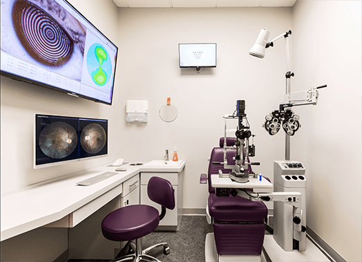 A consulting room with slit lamp and phoropter, diagnostic images of the eye on the screens